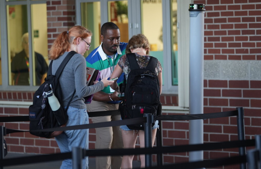 Teacher monitoring students as they pass through a weapon detection system at school entrance